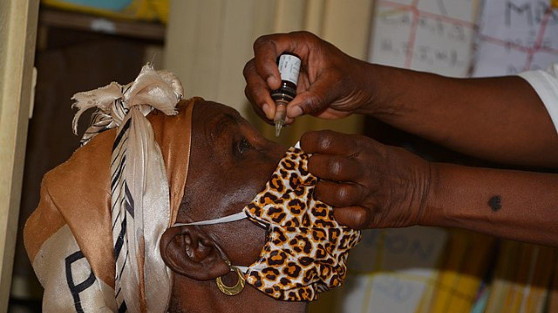 An elderly individual reclining while receiving eye drops, administered by another person's hands