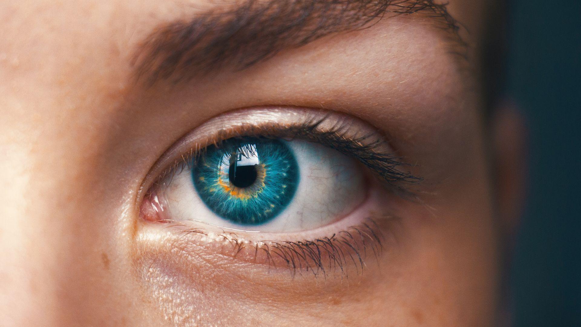 A close-up image of a person's face focusing on one eye, which has a vibrant blue iris with hints of yellow around the pupil