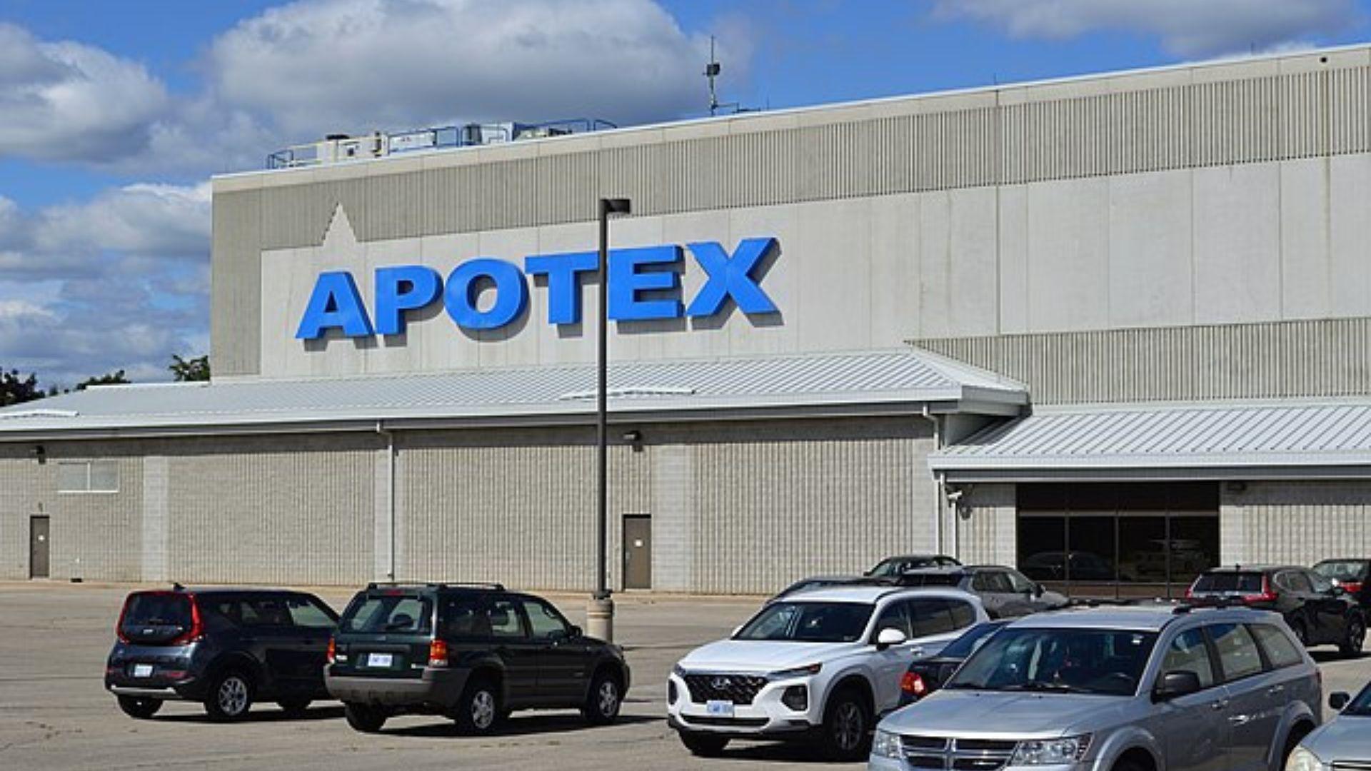 A daytime view of the Apotex facility, a large industrial building with a plain facade, prominently featuring the company's name in large blue letters