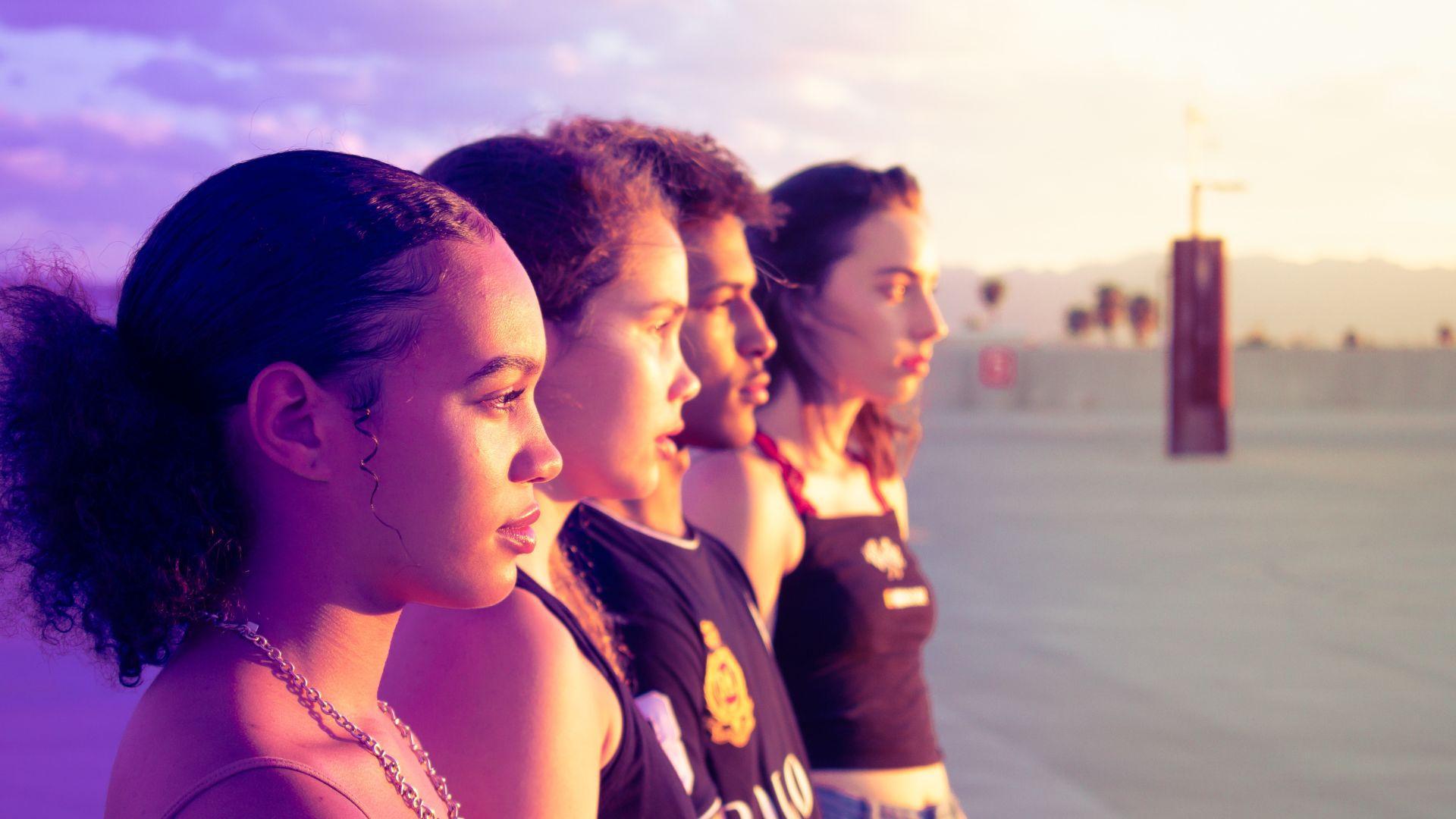A group of four young individuals gazing into the distance during sunset, with their profiles illuminated by the warm, golden light